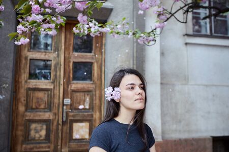 Young woman posing on the background of the old wooden door and blooming sakura