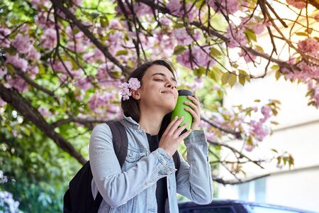 Young smiling happy woman hold green bottle on the background of blooming sakuraの写真素材