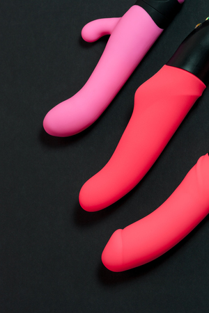 Pink vibrators for girls. Sex toys. Sex gadgets and masturbation devices. Three pink dildo on a black background. View from above. Place for advertising text. View from above. Concept art for sex shopの写真素材