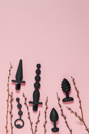 Sex toys. Sex gadgets and masturbation devices. A black dildo, butt plug, anal balls, vibrator and a sprigs of willow on pink paper. View from above. Place for text. Top view. Sex shop conceptの写真素材