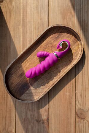Violet unusual vibrator in the form of a rabbit lies on a wooden tray on the table. Dildo for vaginal and clitoral stimulation. Image for the sex shop. Sex toys for adult. Rabbit dildo with vibration.の写真素材