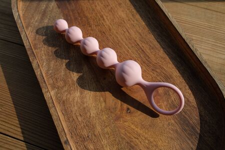 Pink rubber butt plug with a ring lies on a wooden tray on the table. Sex gadgets and masturbation devices for adults. Image for the sex shop. Sex toys for adult. Anal plug of balls of different sizesの写真素材