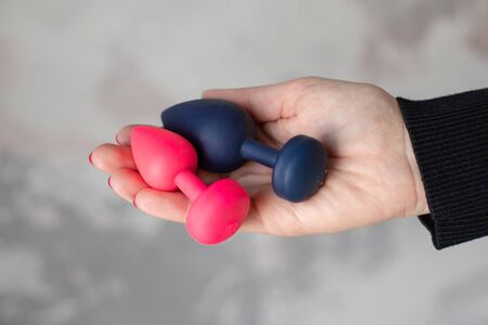 Erotic pleasure toy on a woman hand. Sex gadget and masturbation device for adult. A pink and black rubber  anal plugs in a female hand. Sex shop concept. Woman hand hold sex toys.の写真素材