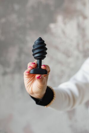Erotic pleasure toy on a woman hand. Sex gadget and masturbation device for adult. A black rubber anal plug in a female hand. Sex shop concept. Woman hand hold sex toys.の写真素材