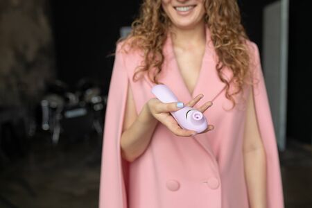 Female hand is holding womanizer sex toys on a pink background. Purple Sex toys in the hand of a woman. Place for text. Sex shop concept. Shop for adults. Minimal dildo vibrator for clitoris.の写真素材