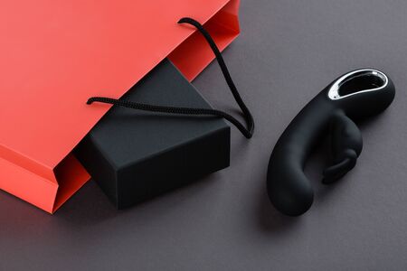 Black rabbit vibrator and a pink paper shopping bag with black box on a grey background. Erotic toy for adult. Sex gadget and masturbation device. Place for text. Sex shop concept.の写真素材