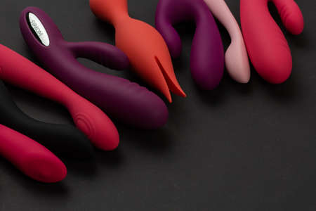 Sex toys and masturbation device. A pink, red, purple and black rubber and silicone dildos is lying on dark paper. View from above. Place for text. Flat lay. Sex shop conceptの写真素材