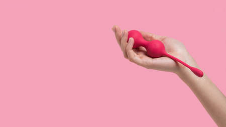 Female hand holding sex toys on a pink background. Kegel balls Geisha balls. Pink vaginal balls in a woman hand. Sex toys for girls. Place for text. Sex shop concept. Copy space. Adult store.の写真素材