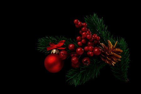 Fir branches adorned with bunches of red berries, a red Christmas ball with a bow and a pine cone painted gold on a black background.の写真素材