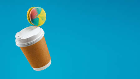 Traditional french macaron and coffee paper cup flying on blue background Macaron or macaroon hang...
