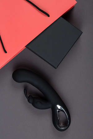 Black rabbit vibrator and a pink paper shopping bag with black box on a gray background. Erotic toy for adult. Sex gadget and masturbation device. Place for text. Sex shop concept.の写真素材