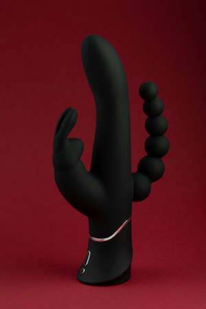 Black sex toy for adult dildo happy rabbit vibrator isolated on red background. Vaginal dildo with vibration. Space for text. Image for the sex shopの写真素材
