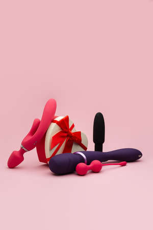 View on a dildos, anal butt plugs, vibrators, vaginal balls and a heart-shaped gift box wrapped in a red bow on a pink background. Valentine's day concept. Sex shop. February 14th. Love day. Sex toysの写真素材