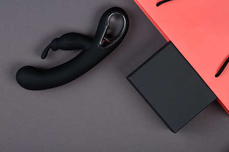 Black rabbit vibrator and a pink paper shopping bag with black box on a gray background. Erotic toy for adult. Sex gadget and masturbation device. Place for text. Sex shop concept.の写真素材