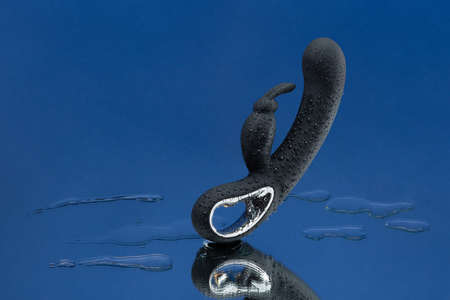 Black vaginal vibrator in drops of water hanging in the air on a dark blue background. Rabbit dildo with vibration. Space for text. Image for the sex shop. Sex toys for adult.の写真素材