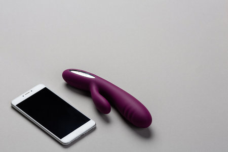 Violet rabbit vibrator and smartphone lie on a gray background. Side view. Place for text. View from above. Sex shop concept. Sex device. Dildo that can be controlled from the phone.の写真素材