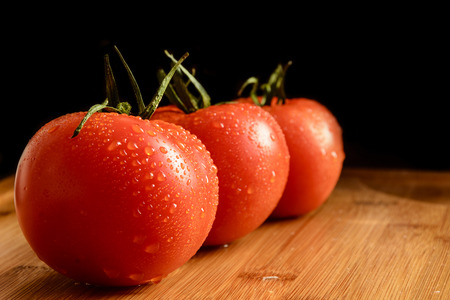 Fresh red tomatoes with drops on a wooden table in a row. Black background.の写真素材