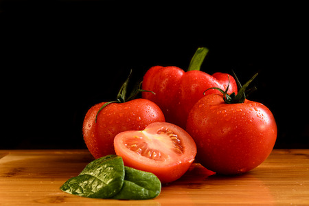 Fresh red vegetables with drops on the wooden table with leaves of spinach. Tomatoes an pepper. Black background.の写真素材
