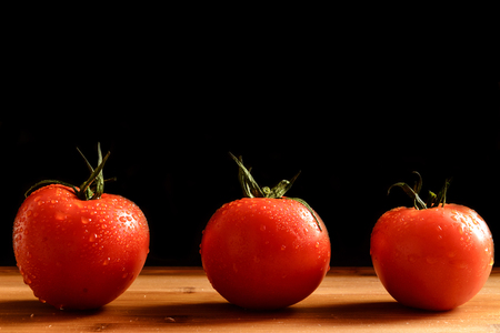 Three tomatoes in a row. Wooden table. Black background.の写真素材