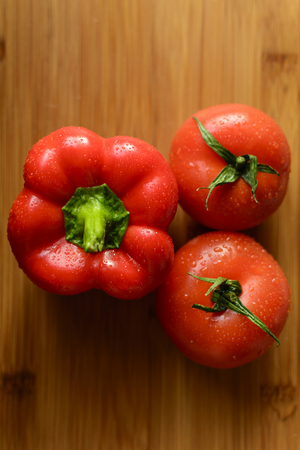 Two tomatoes and pepper on the wooden table.の写真素材