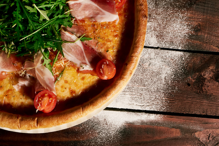Italian pizza with ham, tomatoes and herbs on a wooden table ñlose upの写真素材