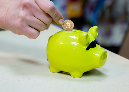 Hand puts bitcoin in a piggy Bank