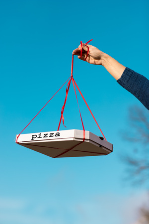 box of pizza in the hand is suspended on a ribbonの写真素材
