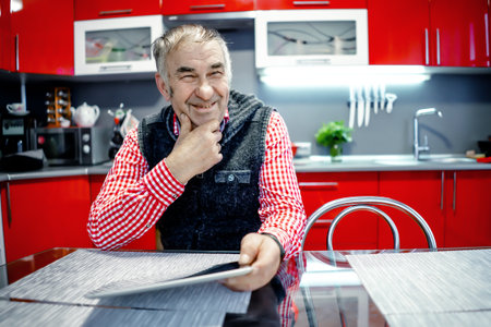 an elderly man with a tablet smiles while sitting at a table.