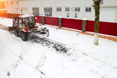 red snow plow tractor clears sidewalks rear view.