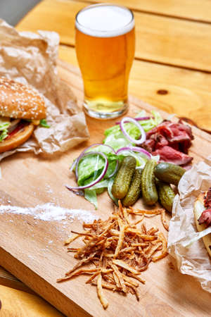 Onion chips, pickles, lettuce, bacon and beer on a wooden boardの写真素材