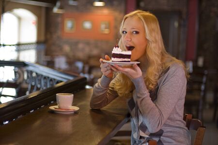 The charming girl drinks coffee with a cake in cafeの写真素材