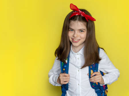 Little beautiful smiling school girl in a school uniform with a backpack. Advertising concept back to school, September 1st, school sale. Portrait on a yellow backgroundの写真素材