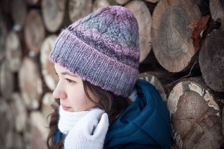 the beautiful young girl in a warm cap from wool of the alpaca in the winter forest. knittingの写真素材
