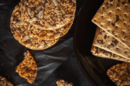 Caramel peanut brittle from sunflower seeds and sesame seeds and fitness cookies with flax seeds on dark black concrete background.の写真素材