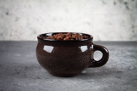 minimalism composition of a round brown ceramic Cup with coffee beans on a gray concrete background