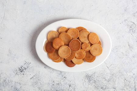 Trendy homemade breakfast, pancake cereal, mini pancakes on white plate on white concrete background