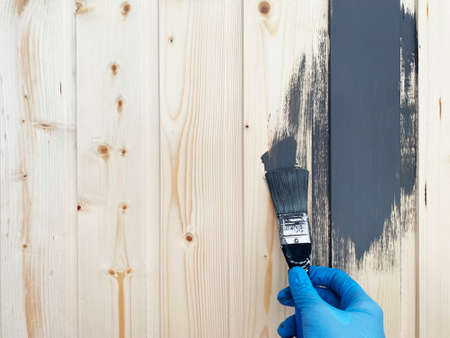 the right hand of worker in blue rubber gloves paints a wooden wall with brush of gray paint. Repair the surface.の写真素材