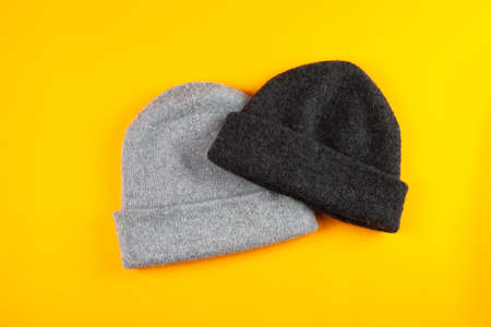 two gray wool Knitted hats on yellow background. spase for text