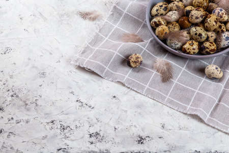 pile of Easter quail eggs on gray fabric cotton rag on concrete background, Round ceramic plate....