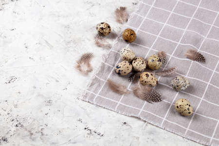 pile of Easter quail eggs on gray fabric rag on white concrete background. space for text