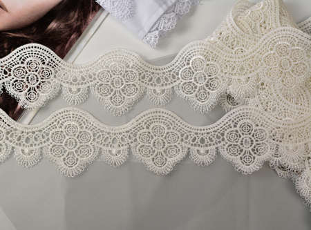 Tapes of ecru white guipure, beauty silk lace fabric on light background. Elastic material. Using...