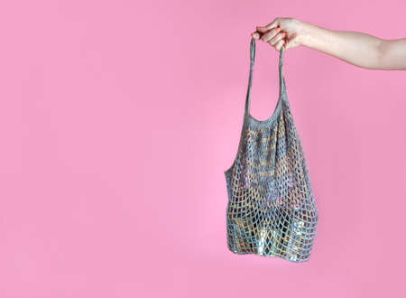 woman's hand holds a gray crochet string bag with tin cans, humanitarian aid, food donation, on a...