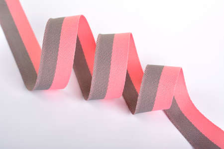 Pink gray Cotton ribbon, roll textilies on bobbin. strapping tape with curl on white background. Use for sewing clothes, bags. Space for text.の写真素材