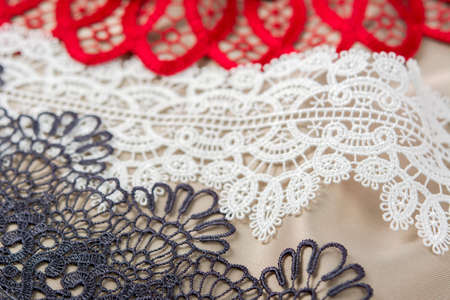 pile of red, white. black and gray gentle luxury quality guipure, lace fabric on beige background....