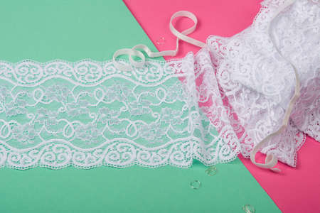 Delicate tapes, gentle ribbon, beauty lace fabric with furniture on pink, green background. Elastic...