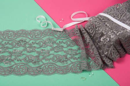 Delicate tapes, gentle ribbon, beauty lace fabric with furniture on pink, green background. Elastic...