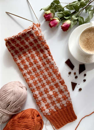 fragment of beige brown sweater, knitted sleeve made of warm sheep wool. white Cup of cappuccino,...
