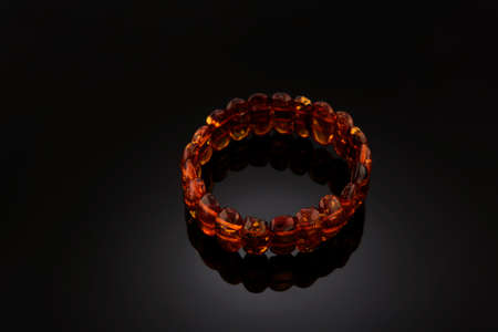 Bracelet made of Natural polished transparent honey luxury amber beads with inclusions on dark black background. shadow with reflection, selective soft focus. Space for text.の写真素材