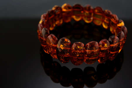 Bracelet made of Natural polished transparent honey luxury amber beads with inclusions on dark black background. shadow with reflection, selective soft focus. Space for text.の写真素材