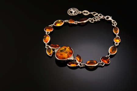 variously sized Bracelet made of Natural polished transparent honey luxury amber beads with inclusions silver hardware and chain on black. close up selective soft focus. Space for textの写真素材